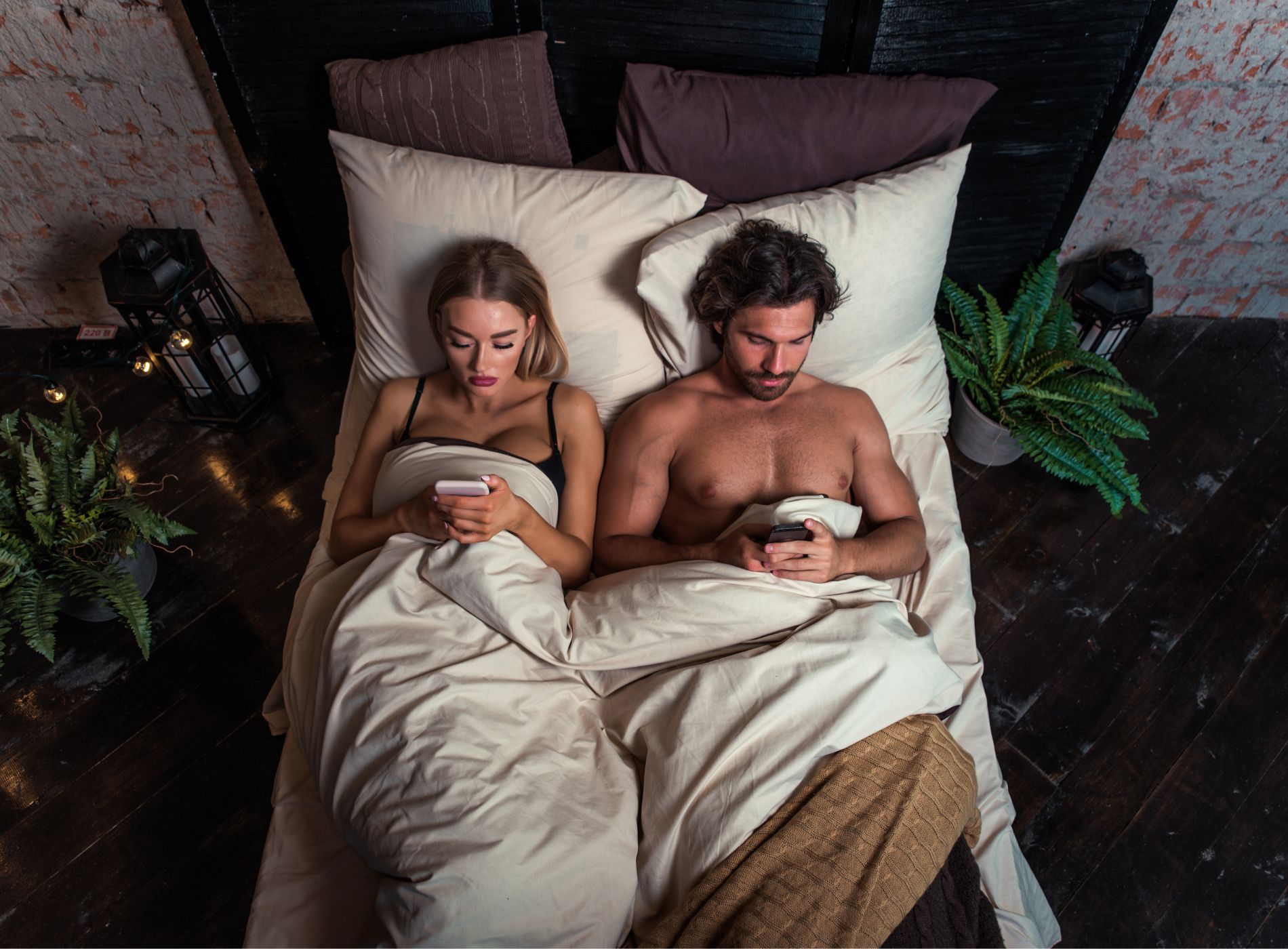 coppia uomo e donna a letto intenti a guardare il proprio smartphone